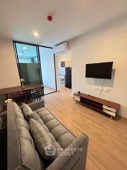 Modern living room with sleek furniture and wall-mounted TV, open to dining area.