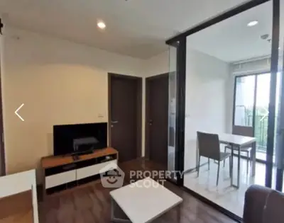 Modern living room with glass partition and dining area, featuring sleek furniture and natural light.