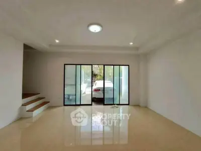 Spacious living room with glass doors leading to a carport, featuring sleek tile flooring and modern lighting.