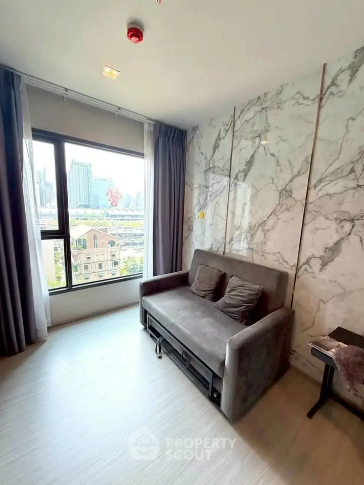 Modern living room with marble accent wall and city view, featuring a stylish gray sofa and large window.