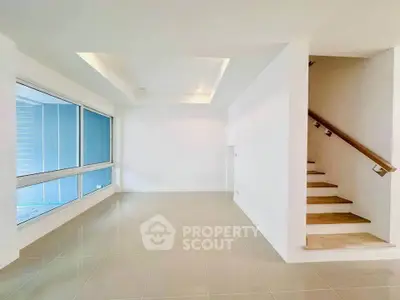 Spacious modern living room with large windows and elegant staircase in a bright, minimalist design.