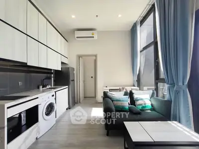 Modern living room with open kitchen, washing machine, and large windows with blue curtains.