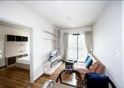 Modern apartment living room with balcony and adjacent bedroom, featuring sleek furniture and wooden flooring.