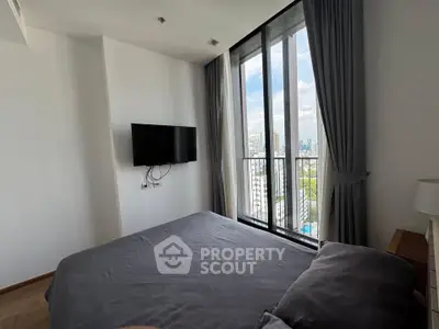 Modern bedroom with large windows offering city views, featuring a wall-mounted TV and elegant curtains.