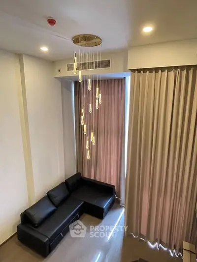Modern living room with elegant chandelier and floor-to-ceiling curtains, featuring a sleek black sofa.