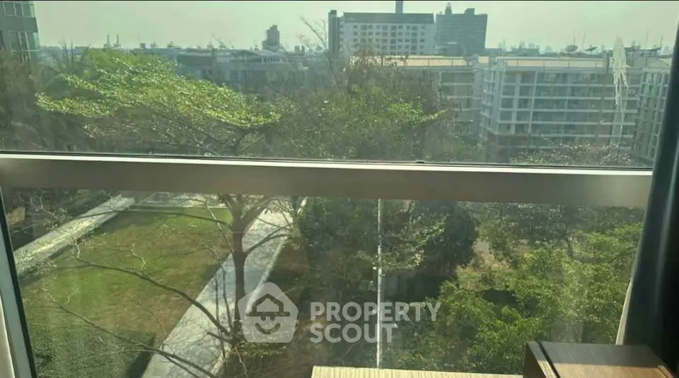 Stunning urban view from high-rise apartment window overlooking lush greenery and cityscape.