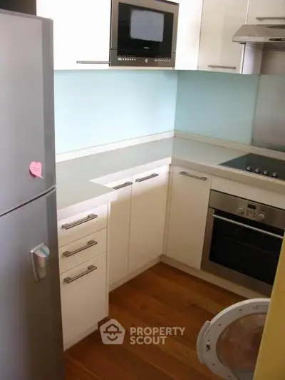 Modern kitchen with sleek appliances and wooden flooring, featuring a built-in oven and microwave.