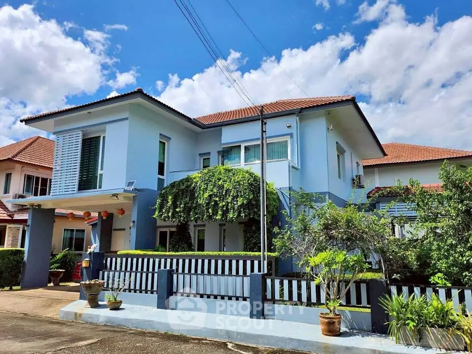 Charming two-story blue house with lush greenery and a sunny sky backdrop, perfect for family living.