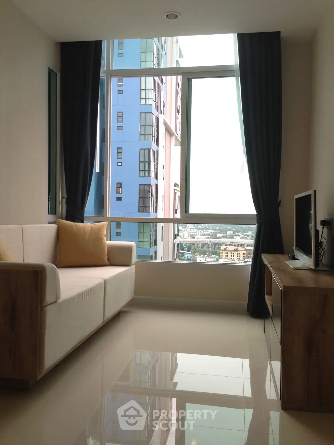 Modern living room with large window and city view, featuring stylish furniture and sleek design.