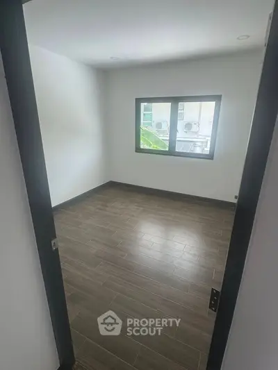 Spacious empty room with large window and modern flooring, perfect for customization.