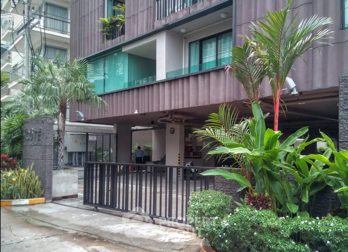 Modern apartment building entrance with lush greenery and secure gated access.