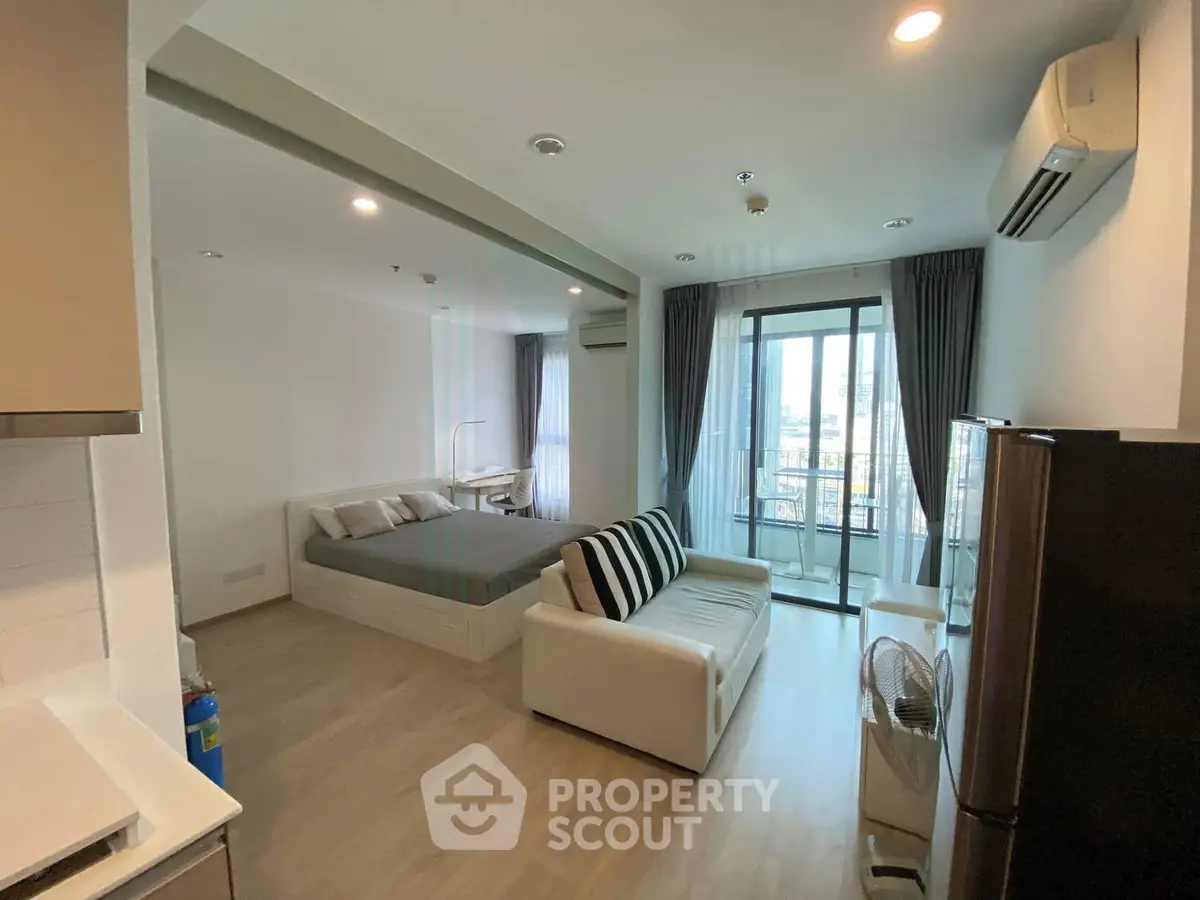 Modern studio apartment with open layout, featuring a cozy living area and a balcony with city views.