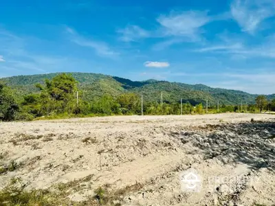 Expansive undeveloped land with potential for construction, offering a serene mountain backdrop and clear blue skies, ideal for a bespoke residential or commercial project.