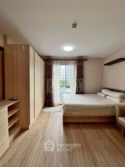 Spacious bedroom with large window and wooden flooring in modern apartment