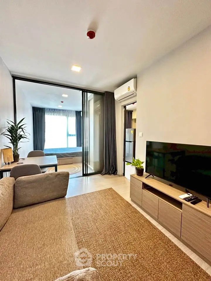 Modern living room with cozy sofa and TV, leading to a stylish bedroom through glass doors.
