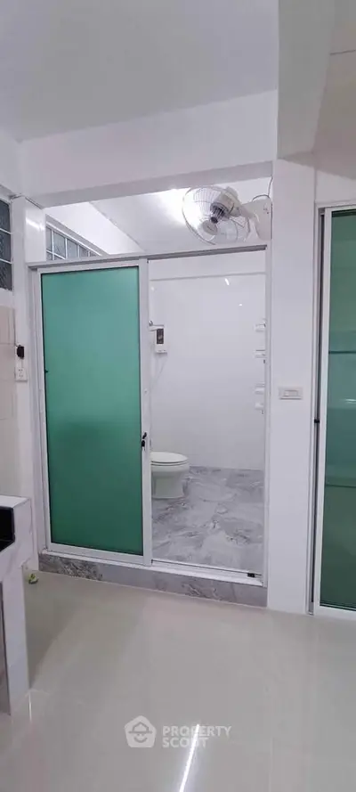 Modern bathroom with frosted glass door and sleek tile flooring in a contemporary home.