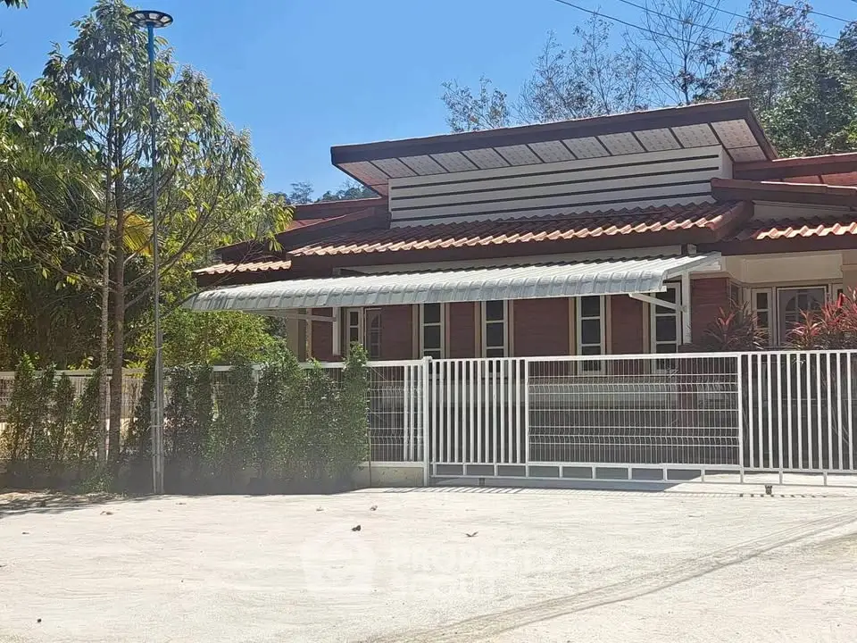 Charming single-story home with modern roof design and spacious driveway, surrounded by lush greenery.