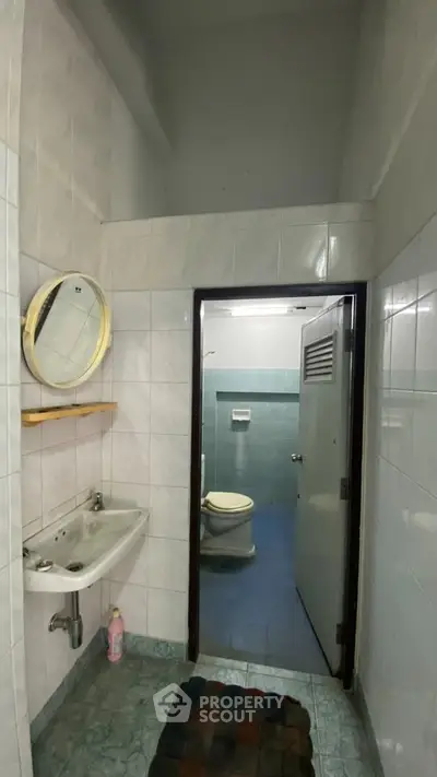 Compact bathroom with tiled walls, sink, and toilet, ideal for small spaces.