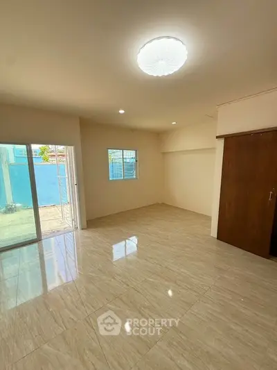 Spacious living room with large windows and sliding door to patio, featuring elegant tile flooring.