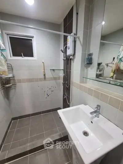 Modern bathroom with sleek sink and shower area, featuring neutral tiles and contemporary fixtures.