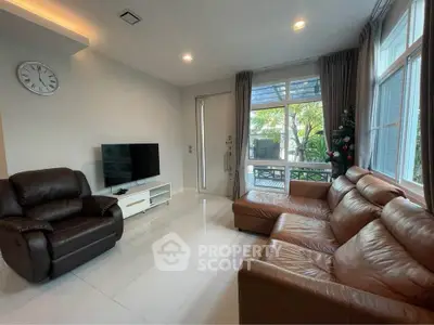 Spacious living room with leather sofas and large windows offering garden view