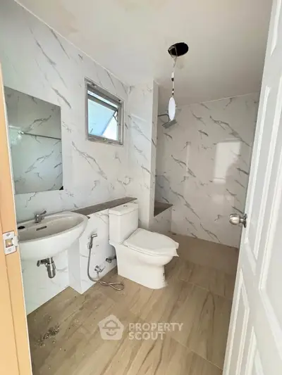 Modern bathroom with marble tiles and wooden flooring, featuring a sleek sink and toilet design.