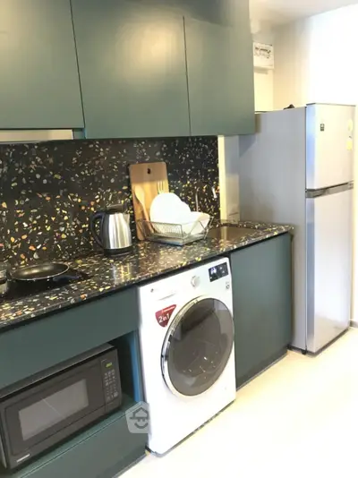 Modern kitchen with terrazzo countertop, washing machine, and stainless steel fridge.