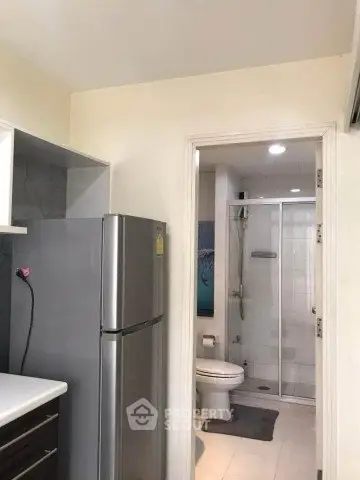 Modern apartment kitchen with stainless steel fridge and view into bathroom with shower.