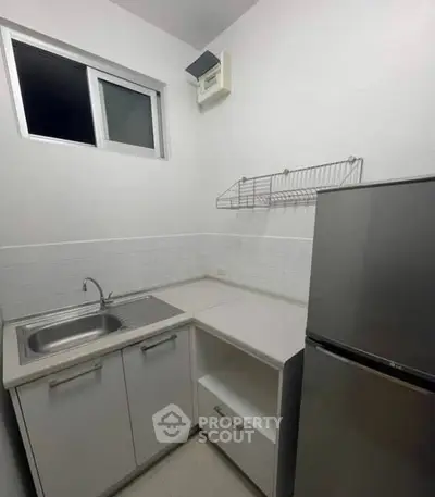 Compact kitchen with stainless steel sink and modern fridge in minimalist design.