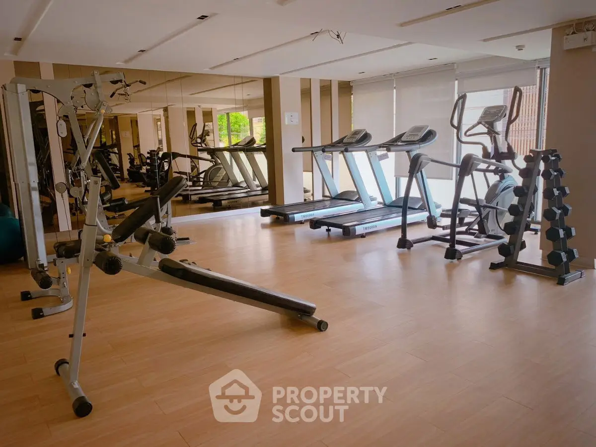Spacious gym with modern equipment and mirrored walls in luxury apartment complex.