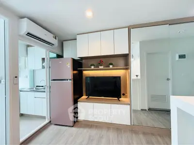 Modern living room with sleek design, featuring built-in cabinets, a TV, and a view into a compact kitchen.
