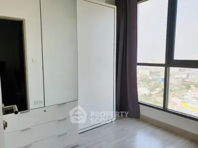Bright bedroom with large window offering city view and sleek white wardrobe.