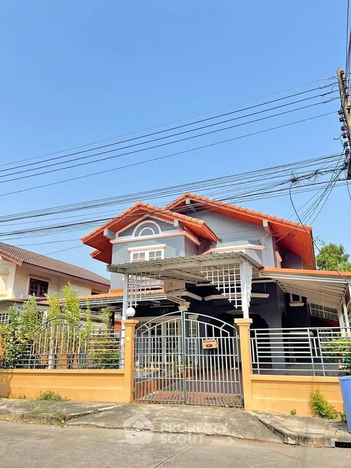 Charming two-story house with gated entrance and vibrant roof in a serene neighborhood.