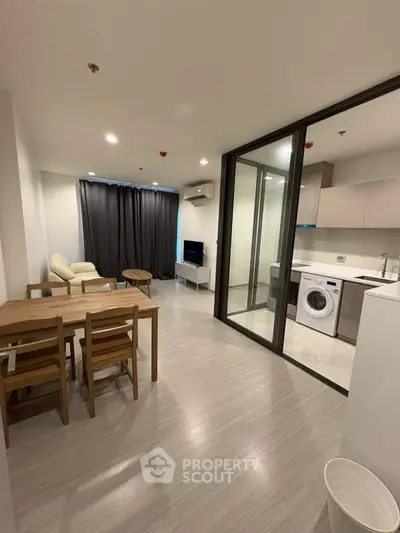 Modern apartment interior with open layout, featuring living area, dining set, and kitchen with washing machine.