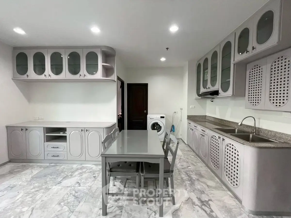 Spacious kitchen with modern cabinetry and dining area, featuring marble flooring and built-in washing machine.