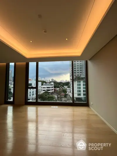 Spacious living room with polished wooden floors and ambient cove lighting, featuring large windows with an urban view, ready for customization.