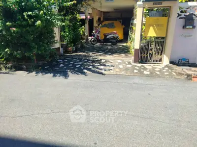 Charming residential entrance with lush greenery and scooter parking