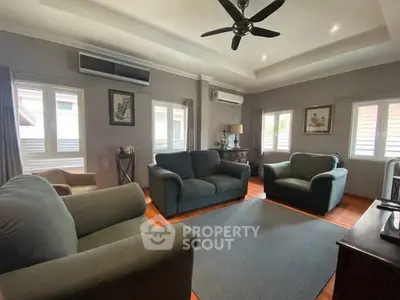 Spacious living room with cozy seating and modern decor, featuring large windows and ceiling fan.