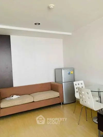Modern living room with cozy sofa, dining set, and fridge in a stylish apartment.