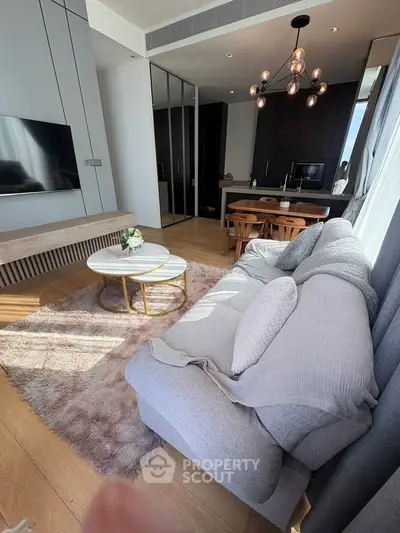 Modern living room with cozy sofa, stylish chandelier, and open kitchen layout in a chic apartment.