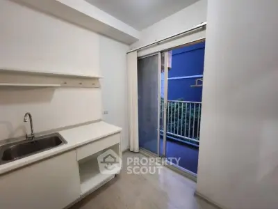 Modern kitchen with sliding glass door to balcony, featuring sleek white cabinetry and stainless steel sink.