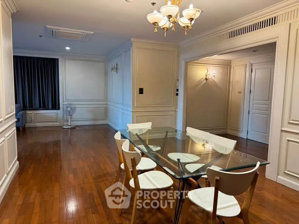 Elegant dining area with glass table and wooden flooring in a spacious apartment.