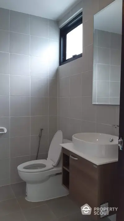 Modern bathroom with sleek design, featuring a wall-mounted sink, toilet, and a small high window for natural light.