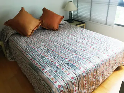 Cozy bedroom with patterned bedspread and natural light from large windows.