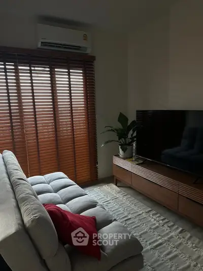 Cozy living room with modern sofa, large TV, and natural light from wooden blinds.