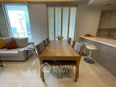 Modern dining area with sleek wooden table and chairs, adjacent to a stylish open kitchen in a high-rise apartment.