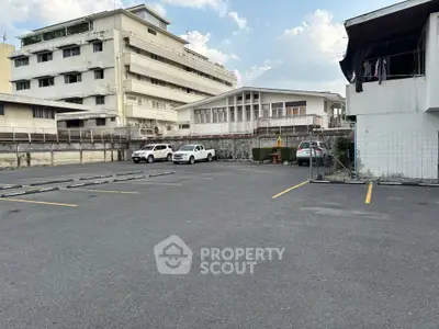 Spacious parking area in urban setting with multiple parked cars and surrounding buildings.