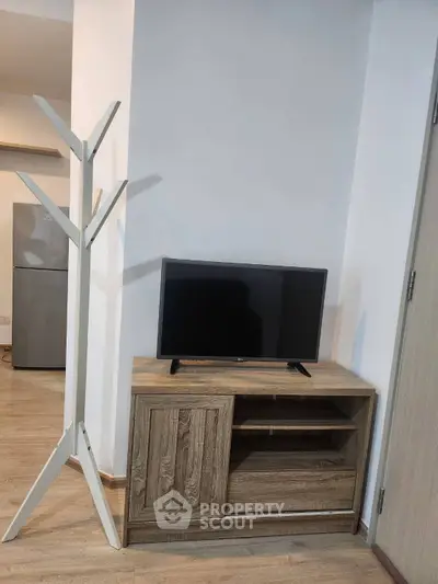 Modern living room with wooden TV stand and sleek coat rack, featuring minimalist decor and light wood flooring.