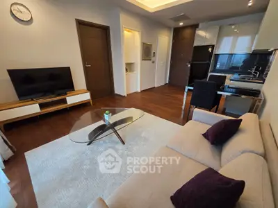 Modern living room with sleek furniture and open kitchen layout, featuring a cozy sofa and glass coffee table.
