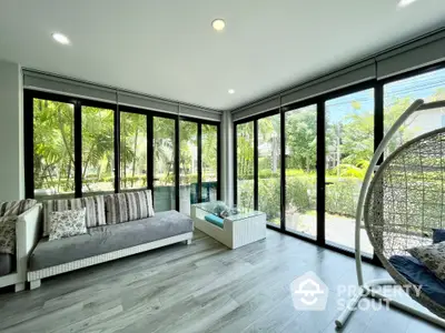 Spacious living room with floor-to-ceiling windows offering lush garden views, complemented by modern furnishings and a stylish hanging chair.